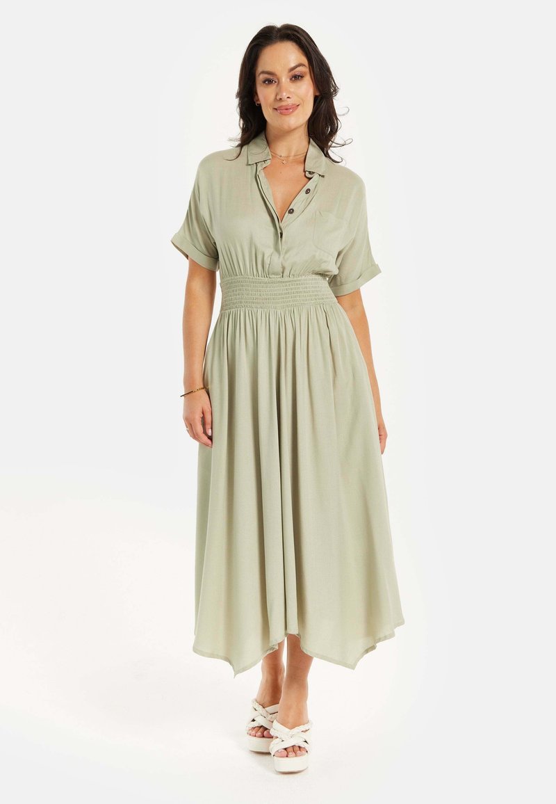 Light green, short-sleeved dress with button details, elastic waist, and flowing skirt. Worn with white, platform sandals.