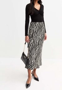 Černý žebrovaný top s dlouhým rukávem v kombinaci s midi sukní se zebrovým vzorem v černé a bílé, černými vysokými podpatky a malou černou kabelkou se zlatými akcenty.