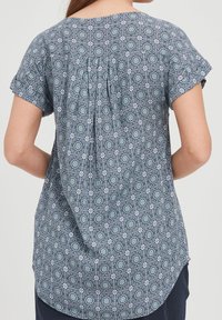 Blusa blu a fantasia con maniche corte, caratterizzata da un motivo floreale e una piega sul retro. Realizzata in tessuto leggero.