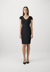 Sydd svart kjole med korte cap-sleeves, V-hals og knelengde. Laget av glatt stoff med minimale sømmer for en strømlinjeformet silhuett.
