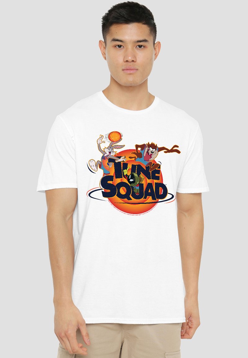 Young man wearing white T-shirt with colorful Tune Squad characters playing basketball and orange basketball logo.