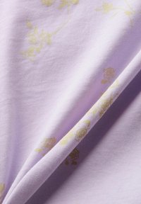 Levandulová látka s jemnou strukturou, která má květinový vzor v zlatých odstínech. Materiál se zdá být hladký a krásně se splétá.