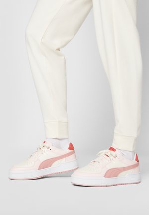 Pink and cream sneaker with a textured upper, round toe, thick white sole, and a coral accent at the heel. Paired with cream sweatpants.