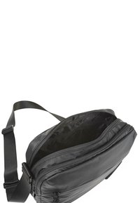 Bolso de hombro negro con cremallera, hecho de material suave. Cuenta con una correa ajustable, forma plana y un amplio interior oscuro.