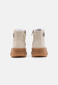 Beżowe zamszowe botki Calvin Klein Jeans za kostkę z brązowymi grubymi podeszwami, widocznym przeszyciem, zamkiem błyskawicznym z tyłu i naszywką z logo na pięcie.