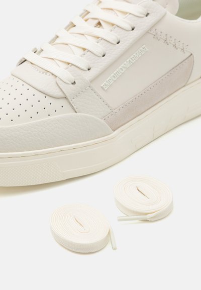 Sneaker en cuir blanc avec un bout perforé, des accents en daim et un branding ton sur ton. Comprend deux paires de lacets crème. Semelle en caoutchouc texturé.