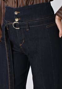 Hoge taille donkerdenim jeans met gouden knoopsluitingen, zij-beltlus, contrasterende oranje stiksels en een getailleerd model met voorzakken.