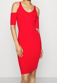 Robe rouge à côtes avec une coupe moulante, dotée de manches froides, d'un décolleté arrondi et d'un ourlet au niveau des genoux. Texture lisse, sans motifs.