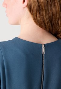 Blue dress with a textured fabric. Features a round neckline and a short zipper detail at the back, accented by silver hardware.