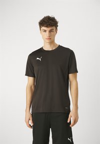 T-shirt atlético preto feito de tecido que afasta a umidade, com gola redonda e um logótipo branco no lado esquerdo do peito. Mangas curtas, textura suave.