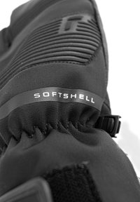 Gant en softshell noir avec panneaux texturés, poignet élastique et une sangle sécurisée. Étiquette gravée "SOFTSHELL" visible.