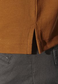 Brauner Baumwollstoff mit strukturiertem Gewebe, mit einem seitlichen Schlitzsaum. Grauer Stoff sichtbar darunter, was einen Lagen-Effekt erzeugt.