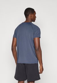 Ναυτικό αθλητικό t-shirt με κοντά μανίκια, λεία υφή και στρογγυλή λαιμόκοψη, συνδυασμένο με μαύρες βερμούδες, ορατό από την πίσω πλευρά.