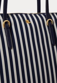 Τσάντα ώμου με κάθετες ρίγες σε ναυτικό μπλε και λευκό, με λαβές από δέρμα σε ναυτικό μπλε και μικρό  χρυσό λογότυπο "RL" κοντά στο πάνω κέντρο.