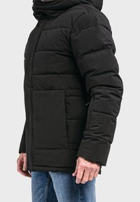 Giacca a vento nera con cappuccio, caratterizzata da un design trapuntato, bottoni a pressione e tasche laterali. Il materiale appare liscio con una leggera lucentezza.