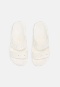 Bele sandale za plažo v beli barvi z dvema širokima trakoma, ki imata krožne izreze in teksturirano podplato za oprijem. Narejene so iz lahkega, prilagodljivega materiala.