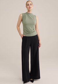 Lichtgroene mouwloze top met geplooid detail, gecombineerd met hoge zwarte wijde broek en zwarte puntige hakken.