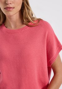 Pull léger rose à manches courtes avec un col rond côtelé et une texture douce, offrant une coupe décontractée et un design minimaliste.