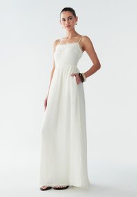 Vestido maxi blanco con tirantes finos, tejido texturizado y encaje en el escote y el dobladillo. Cuenta con un bolsillo lateral y un corte holgado.