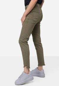 Khaki skinny džíny s roztrhanými lemy, s kapsami na zadní straně a přiléhavým střihem, doplněné o světle šedé tenisky.