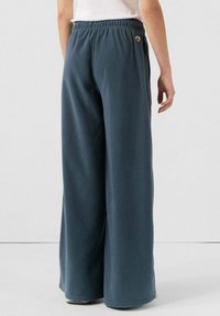 Donkerblauwe fleecetekstuur wijde broek met een elastsiche tailleband. De achterkant heeft een klein logo-opdruk nabij de taille. Zachte textuur.