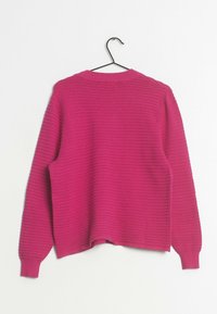 Pull à manches longues côtelé rose vif accroché sur un cintre noir, vu de dos sur un fond blanc.