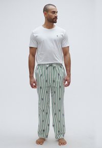 Bijela pamučna majica s malim logotipom, uparena s hlačama zeleno-bijelih okomito prugastih uzoraka koji se ponavljaju i remenom za vezanje u struku.