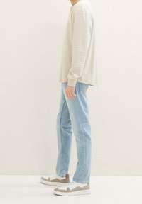 Langärmliges, hellbeiges gestreiftes Hemd kombiniert mit hellblauen Jeans und grau-weißen Sneakers, zeigt einen entspannten Schnitt und einen lässigen Stil.