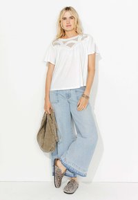 Haut blanc à manches courtes avec des détails transparents, jean large bleu clair, et chaussures à glissière imprimé léopard ; tenant un sac gris.