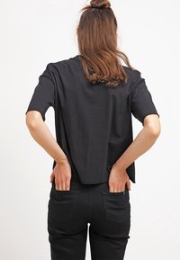 Černé tričko s krátkým rukávem a volným střihem, s kulatým výstřihem, v kombinaci s černými džíny, které mají dvě zadní kapsy.