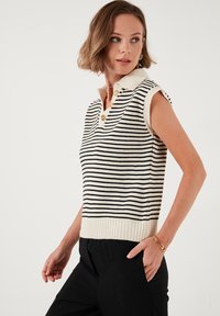 Mouwloze gebreide polo in crème met zwarte strepen, met een geribbeld zoom en een placket met drie gouden knopen en een contrasterende kraag.