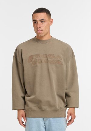 Hanorac supradimensionat de color olive, realizat dintr-un material moale, cu un design de logo reliefat într-o nuanță mai închisă și cu manșete și tiv zimțat.