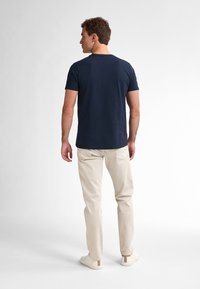 Námořnická modrá bavlněná tričko s kulatým výstřihem, krátkými rukávy, spárováno s krémovými kalhotami a světlými botami.