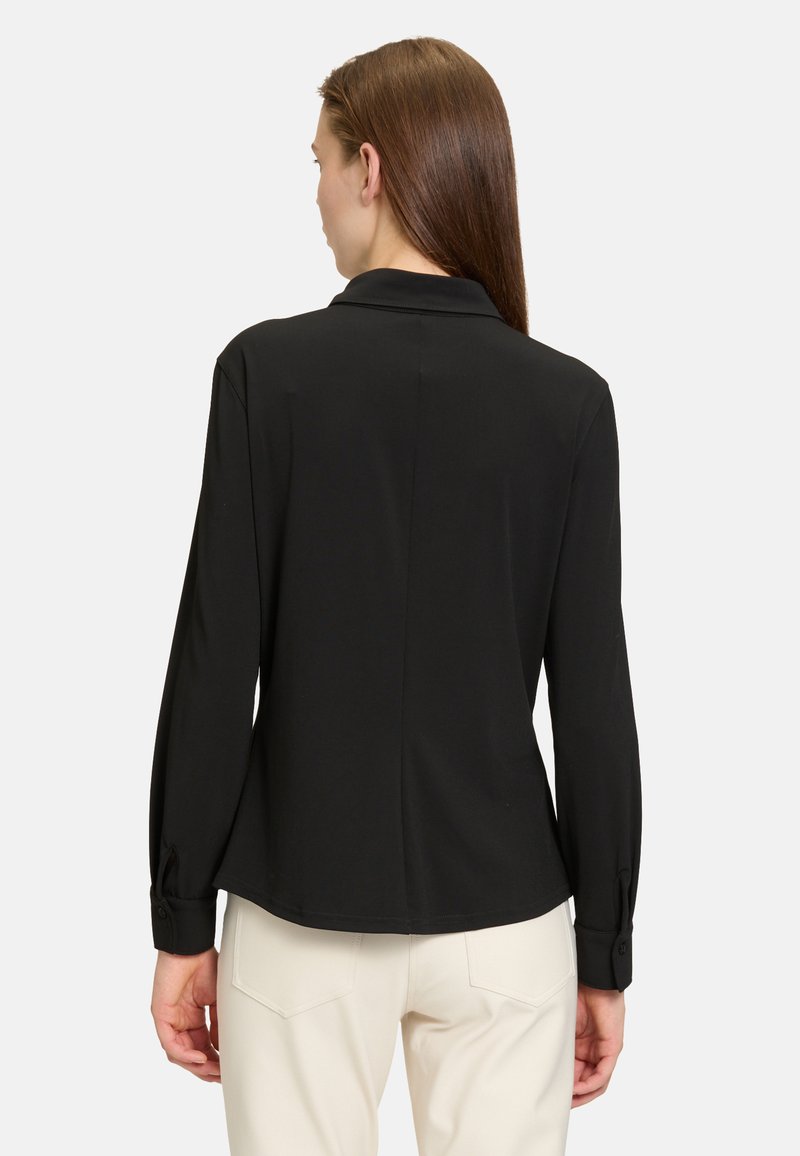 Black long-sleeve blouse with a collared neck, smooth fabric, and buttoned cuffs. Features a back seam and simple design.