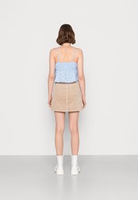 Top cropped azul claro com padrão floral e alças finas, combinado com uma saia mini de veludo cotelê bege. Modelo a usar botas brancas até ao tornozelo.