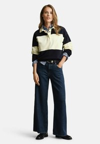 Marineblauw en crème kleurgeblokkeerde lange mouwen polo, gecombineerd met wijde donkerdenim jeans. Ontspannen pasvorm, met een kraag en knoopdetails.