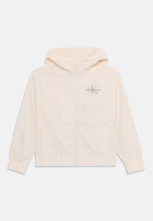 Šviesiai kreminė zip-up striukė su kapišonu, elastingais rankogaliais ir šoninėmis kišenėmis. Su "Calvin Klein Jeans" logotipu pilka spalva ant krūtinės.