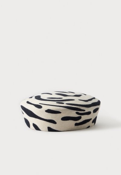 Béret rond en laine avec un motif de rayures zèbre noir et blanc sur un fond blanc uni.
