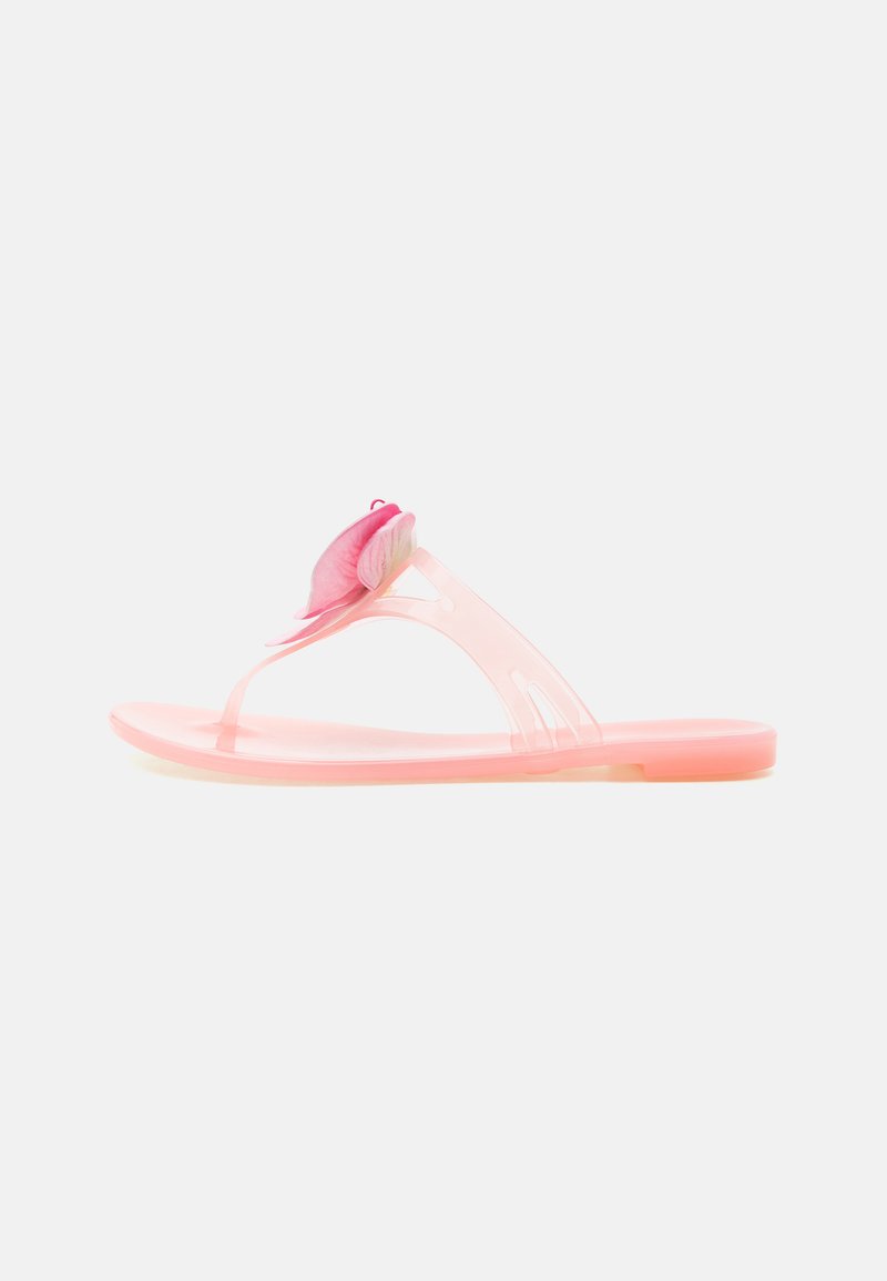 Sandale plate translucide rose avec bride entre les orteils ornée d’une grande décoration papillon rose sur fond blanc.