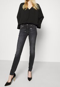 Musta paita nappien kanssa, korkea vyötärö tummat farkut koristellulla edellä, ja mustat kärkitossut. Yksinkertainen muotoilu, istuva malli.