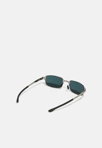 Μεταλλικά γυαλιά ηλίου με σκούρους πράσινους φακούς, ορθογώνιο σχήμα, ασημένιοι σκελετοί και μαύρες καουτσούκ ταπές. Μινιμαλιστικός σχεδιασμός χωρίς σχέδια.