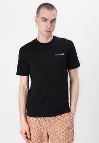 Czarny bawełniany t-shirt z krótkimi rękawami, okrągłym dekoltem, z białym napisem "Paris French Sportswear" na klatce piersiowej. Gładka tekstura.