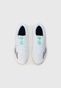Hvide atletiske sneakers med mesh-tekstur, sorte accenter og et grønt mærke. Har snørebåndslukning og polstret sort indersål.