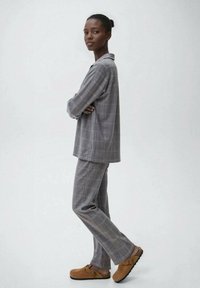 Conjunto de ropa de cama de cuadros grises con una parte superior de corte holgado y cuello, y pantalones de pierna recta, combinados con zuecos marrones con detalle de hebilla.