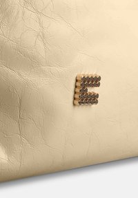 Beige leren tas met een opvallend metalen "E"-accent, bestaande uit afwisselend glanzende en matte cirkelvormige elementen.