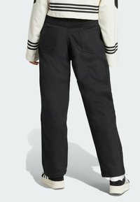 Pantalones negros de pierna ancha con una textura suave, que cuentan con dos bolsillos traseros. Combinados con zapatillas negras y blancas, y una chaqueta recortada.