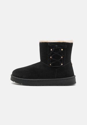 Botín negro de ante con forro de piel sintética, parte frontal con cordones, ojales en tono dorado y suela gruesa de goma negra.