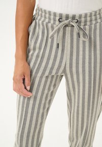 Pantaloni za jogiranje s prugicami v bež in črni barvi, z raztegnjenim pasom, nastavljivim vrvico in ribjo kostjo.