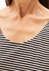 Tessuto a righe bianche e nere con scollo ampio a barchetta. La texture è morbida, mostrando una finitura liscia e sottili macchie nel materiale.