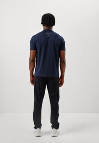 Navy blue short-sleeve t-shirt with a crew neck, smooth texture, subtle logo detail on the back, paired with black loose-fit pants and white sneakers.